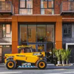 JCB 505-20E Telescopic Handler transporting pallet of plants in front of building.