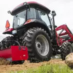 Mahindra 6075 cab utility tractor driving up a hill.