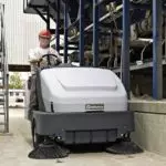 Advance Proterra rider sweeper cleaning ground outdoors along railing.