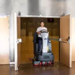 Advance SC4000 ride-on scrubber driving through doorway.