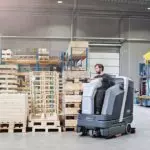Operator cleaning warehouse floors with Advance SC6000 rider scrubber.