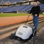 Advance Terra 28B walk-behind sweeper cleaning fallen items off the ground at a baseball stadium.