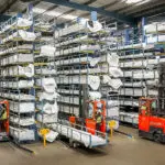 Combilift C6000 ST Stand On Multi-Directional Forklifts carrying materials in warehouse.