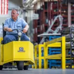 Worker driving Cushman Minute Miser in warehouse aisle.