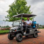 2 people driving in Cushman Shuttle 2+2 personnel carrier.