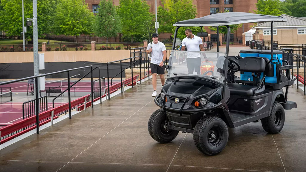 Tennis players walking to Cushman Shuttle 2+2 personnel carrier.