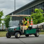 Maintenance worker driving Cushman Shuttle 2 utility vehicle with materials in the bed.