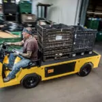 Worker driving Cushman Titan XD burden carrier in warehouse with crates on cargo deck.