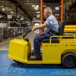Cushman Minute Miser electric burden carrier driving through warehouse.