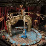 Worker raised in Genie AWP-25S Aerial Work Platform in an indoor stage area.