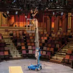 Worker repairing lighting in raised Genie AWP-25S Aerial Work Platform.