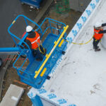 Operators working with Genie Boom lift with fall arrest bar accessory installed.