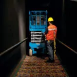 Worker walking behind Genie GS-3232 scissor lift in hallway.