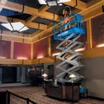 Genie GS-3232 with worker in bucket raised to the ceiling.