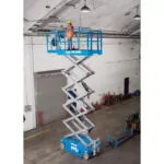 Genie GS-3246 slab scissor lift with worker in bucket raised to ceiling.