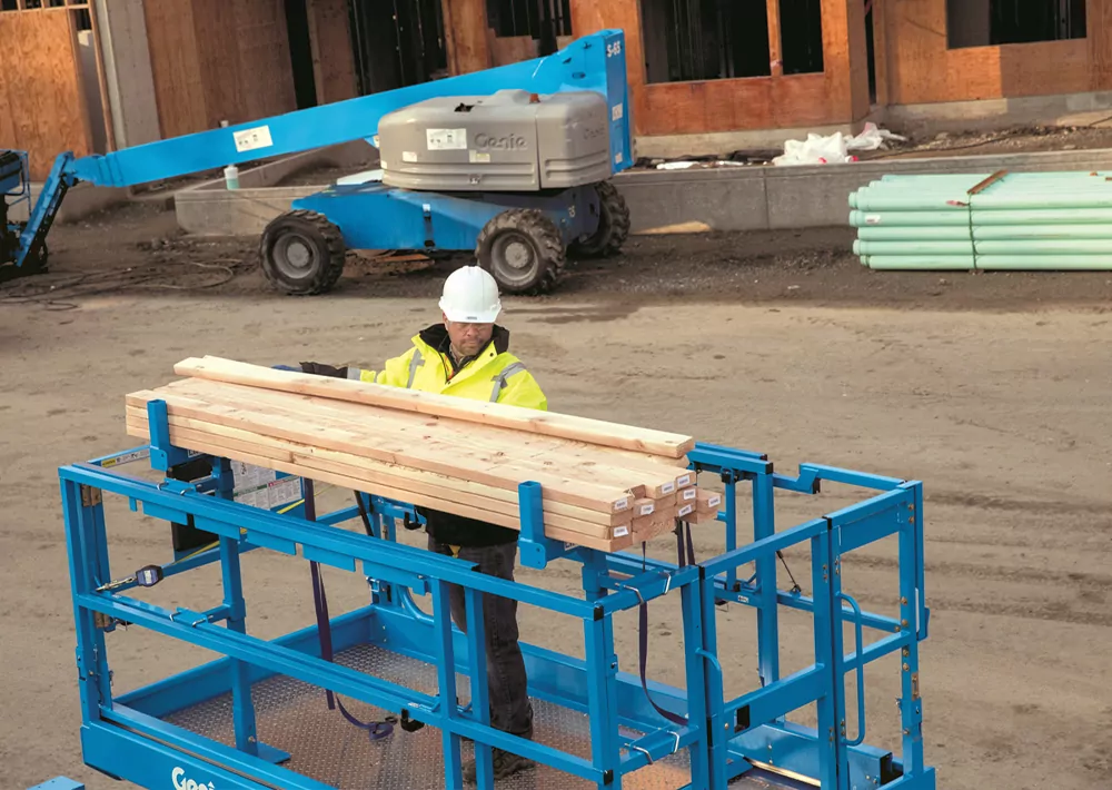 Man in genie lift bucket transporting lumber with material carrier attachment.