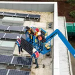 Workers lifting solar panels on a roof on Genie S-40 XC telescopic boom lift work platform.