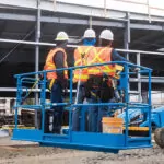 Workers driving Genie S-40 XC telescopic boom lift in outdoor construction site.