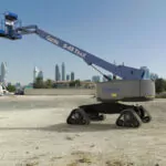 Genie S-45 XC TraX telescopic boom lift driving on sandy terrain.