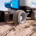 Genie S-85 HF boom lift wheels on rough dirt terrain.