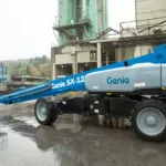 Worker driving Genie SX-125 XC telescopic boom lift outdoors in the rain.