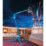 Worker raised in Genie TZ-34/20 trailer-mounted boom lift indoors.