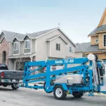Genie TZ-50 trailer mounted boom lift being pulled behind a truck in a residential area.
