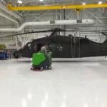 Employee cleaning helicopter shop floors with IPC Eagle CT160 rider scrubber.