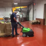Worker cleaning shop floors with IPC Eagle CT30 walk-behind scrubber.