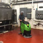 Employee cleaning manufacturing facility floors with IPC Eagle CT51 walk-behind scrubber.