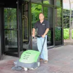 Man sweeping outside entryway with IPC Eagle SmartVac 464 walk-behind sweeper.