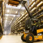 JCB 55-28G Teletruk lifting pallet of materials onto shelf in warehouse.