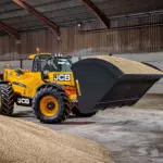 JCB 560-80 Agri Plus telescopic handler with bucket attachment transporting materials.