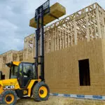 JCB 940 rough terrain forklift lifting lumber on top of building under construction.