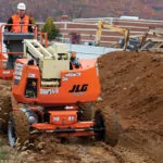 Construction worker driving JLG 340AJ Articulating Boom Lift across dirt hill.