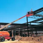 JLG 400S telescopic boom lift raising workers on construction site.
