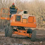 JLG 400S telescopic boom lift driving on rough dirt terrain.