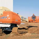 JLG 660SJC telescopic crawler boom lift driving through rough dirt terrain on jobsite.