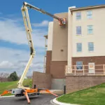 JLG X770AJ boom lift raising worker to perform building maintenance.