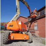Back of JLG H340AJ Hybrid boom lift on gravel road at outdoor job site.