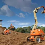 JLG H340AJ Hybrid articulating boom lifts driving on dirt hill.