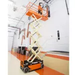 JLG R1932 electric scissor lift raising a worker in a warehouse.