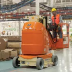 JLG 26E boom lift lowered and driving in warehouse manufacturing facility.