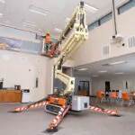 JLG X500AJ compact crawler boom lift extended to building ceiling.