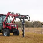 Mahindra 2638 compact utility tractor with cab: auger attachment digging into grass field.