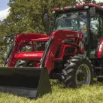 Mahindra 6075 utility tractor with cab parked in grass field.