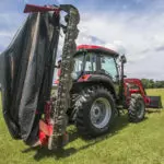 Mahindra 6075 cab tractor driving through grass field.