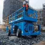 Construction worker driving Genie GS-4390 scissor lift on rocky road.