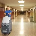 Operator riding on Advance SC1500 scrubber, cleaning floors in a school hallway.