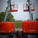 Back of Skyjack SJ45 AJ+ articulating boom lifts with raised jibs next to a rainbow.
